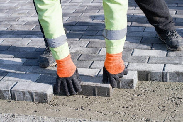 Concrete contractor placing brick pavers by hand for residential driveway installation in Beachwood, OH