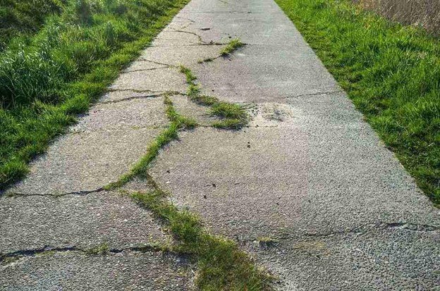 Cracked and damaged concrete driveway with visible wear and weeds growing through the surface in Chagrin Falls, OH